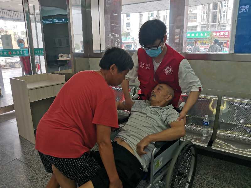 02图为就诊患者因伤情较重，不能行走，志愿者协助其家人将患者抬上轮椅。皖南医学院姚忻提供